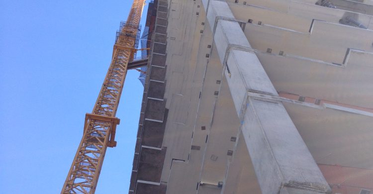 A view of a tall building from the ground with a crane on the left